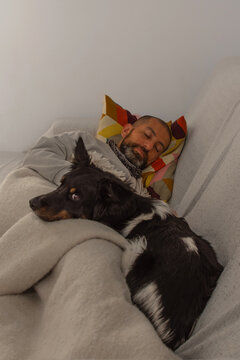 Adult man sleeping on couch with dog resting beside him at home