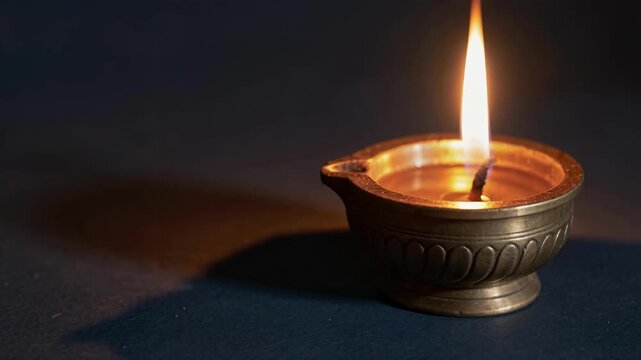 Close up of a Lit Traditional Oil Lamp Flickering Gently on Dark Blue Surface Creating Warm Ambient Lighting for Meditation or Spiritual Rituals