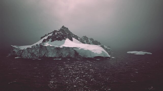 Iceberg emerging through heavy fog on quiet ocean, eerie silence and subdued palette convey melancholy, solitude and atmospheric editorial mood.
