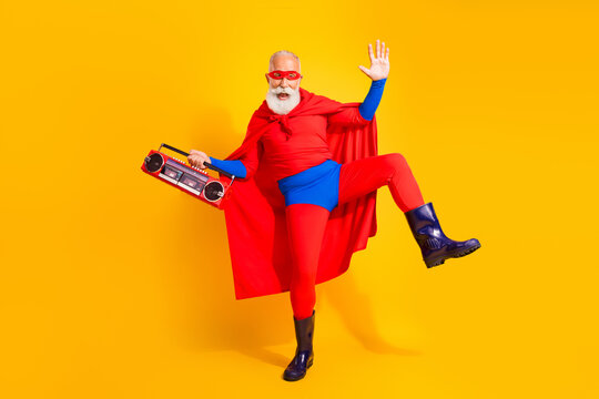 Energetic super hero performer in bright red and blue costume cape dancing with a boombox against a vibrant yellow background
