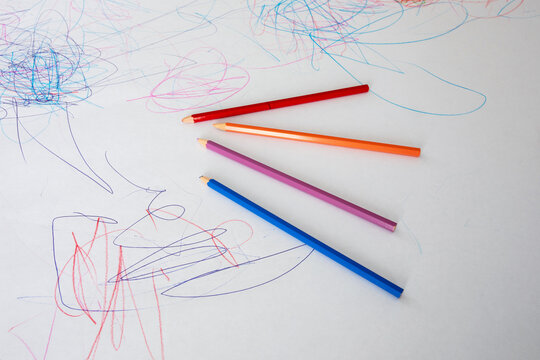 Colorful unsharpened wooden pencils lying on a white paper surface covered with child scribbles and drawings