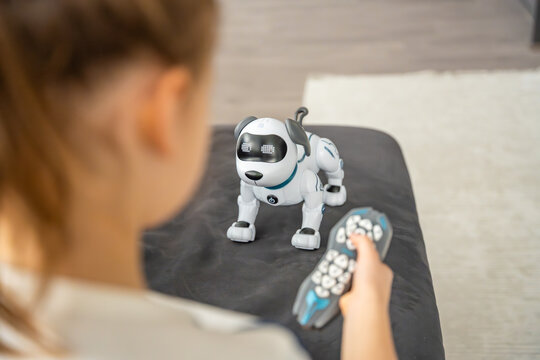 Child controlling robotic dog with remote controller while sitting on sofa at home. Artificial intelligence technology in everyday childhood and smart toy interaction.