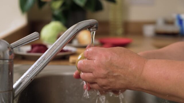 Rinsing potato under running water preparing Ukrainian borscht. Washing tuber cleaning dirt before adding to national soup of Ukraine. Scrubbing fresh potato making base ingredient for traditional