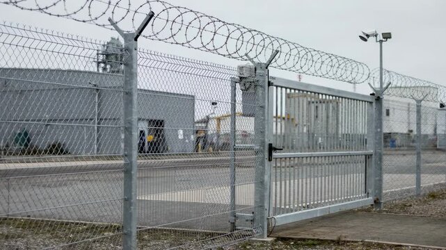 Medium shot of chainlink perimeter fencing securing an industrial explosive plant highlighting tough metal mesh and controlled entry points.