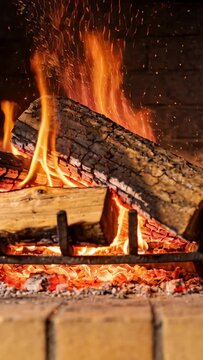 Vertical video: Crackling embers igniting top log on grate, feeding taller flame in hearth, sparks
