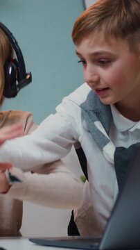 Caucasian boy and girl playing game on laptop and tablet device together with smile face at home in games room. Jojful children sitting the table play online video games and browsing social media in