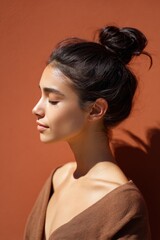 Fototapeta premium Female hispanic young profile portrait with topknot bun terracotta background closed eyes serene natural light soft skin minimalist styling