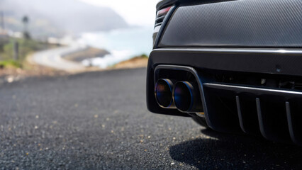 Sports car with carbon fiber body and titanium exhaust pipe on coastal road. Automotive customization and performance tuning concept. Modern vehicle engineering and racing aesthetics.