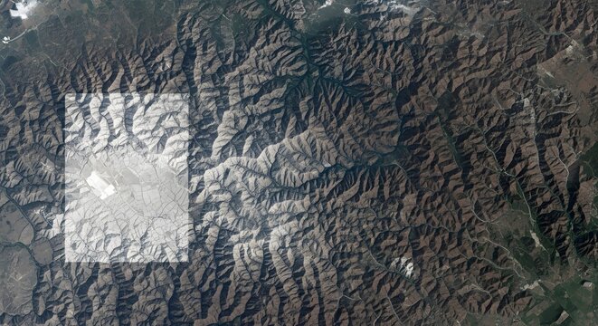 Satellite view of a mountainous region featuring a bright, high-contrast rectangular data overlay