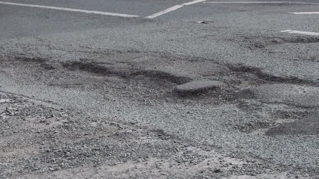 Cars driving over potholes on a damaged asphalt road