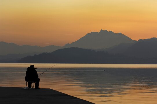 Fisher by sunset at the Zugersee with the Pilatus in the background, Zug, Switzerland