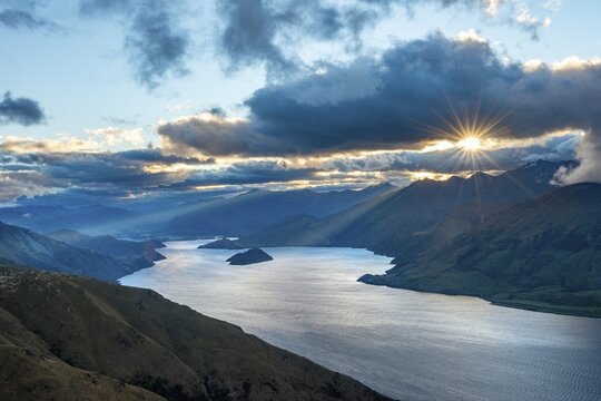 Last rays of sun shining through cloudy sky, view of Lake Wanaka at sunset, lake and mountain landscape, view from Isthmus Peak, Wanaka, Otago, South Island, New Zealand