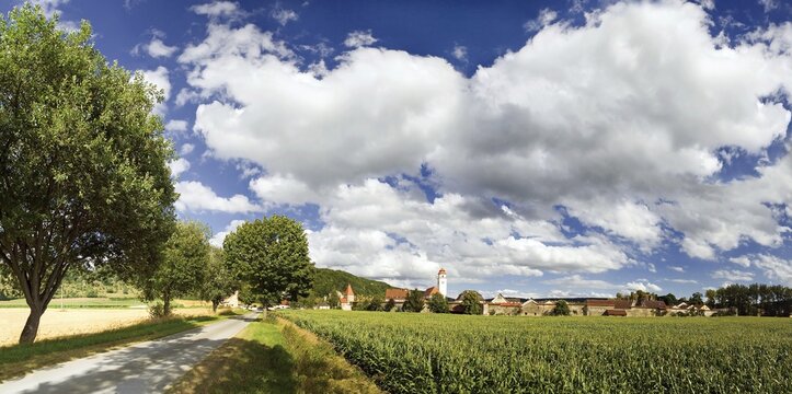 Wide angle photo of the Dollnstein market town behind a maize field and country lane and under unusual cloud formations in the Altmuehltal Nature Park, Bavaria, Germany, Europe