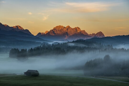 Mountain meadows with small huts in light ground fog and Zugspitz massif in the background at sunrise, Kr&uuml;n, Bavaria, Germany