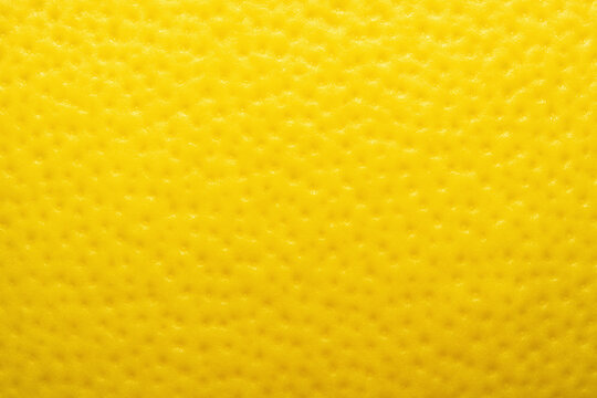 Fruit skin surface made of citrus peel in bright yellow tones with a porous pitted texture in a full frame macro.