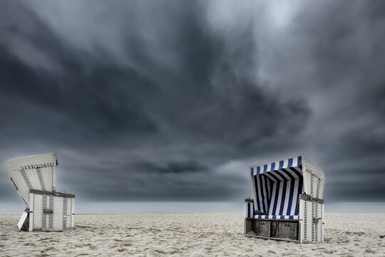 Beach chairs in front of dark cloudy sky, Kampen, Sylt Island, Germany