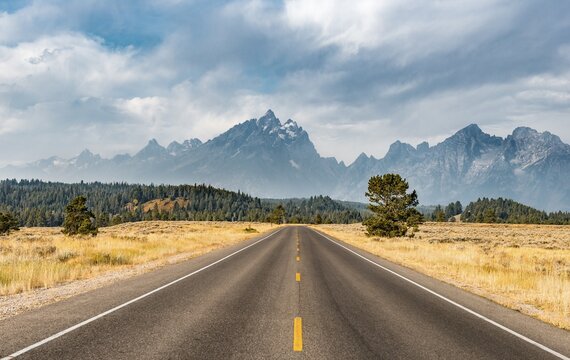 Highway in front of rugged mountains with cloudy skies, Grand Teton Range, Grand Teton National Park, Wyoming, USA