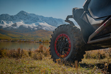 Close up of UTV and  ATV off-road vehicle wheel on autumn grass with scenic snow mountains and lake background. © ANDREY