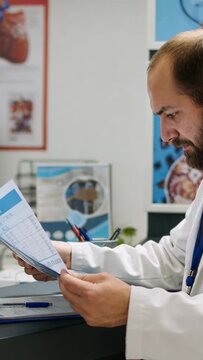 Clinician picking up brain scan film and cross-checking slices with printed report for diagnosis