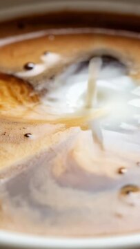 Vertical milk stream pouring into black coffee cup, forming crema vortex and blending into marble