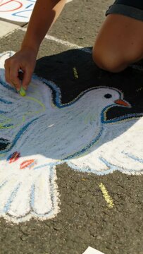 Vertical video: Placing yellow chalk, artist kneeling on lot in blue top, shorts, shading dove wing