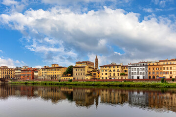 Fototapeta premium The Arno River Embankment reveals charming architecture in Florence, Italy. Colorful buildings line the water, reflecting the vibrant skyline under a blue sky.