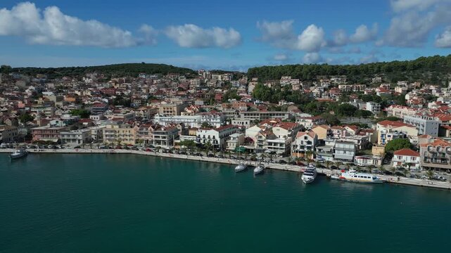 Coastal town with colorful buildings and boats docked in a turquoise bay under a blue, cloudy sky.