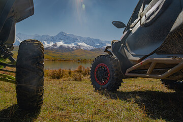 Close up of UTV off-road vehicles parked on a meadow by a mountain lake with snow peaks. Expedition, extreme adventure travel and overlanding concept. © ANDREY