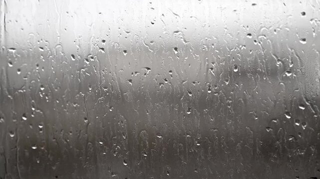 Raindrops slide down a wet window pane. Blurred background suggests rainy day outside. Moody atmosphere, perfect for intros or cinematic scenes