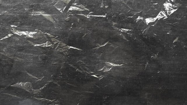Abstract dark surface with crinkled transparent plastic texture in motion