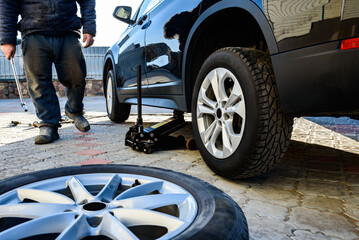 Changing wheels and tires for a car according to the season. A man unscrewing and removing the wheels in the yard. © Natallia