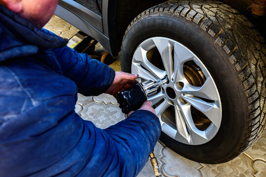 Changing wheels and tires for a car according to the season. A man unscrewing and removing the wheels in the yard.