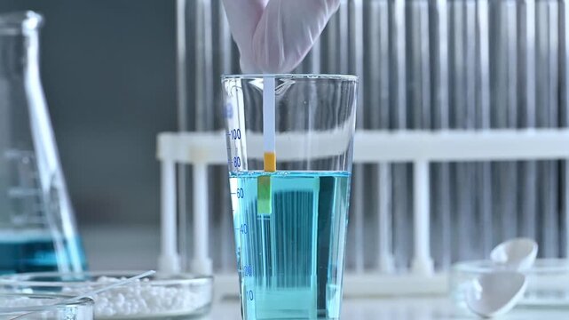 A chemist scientist tests the acidity of a liquid in a petri dish using litmus paper in a laboratory.