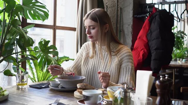 young beautiful woman eats borscht with spoon in cafe, girl eats soup with lard and bread in restaurant