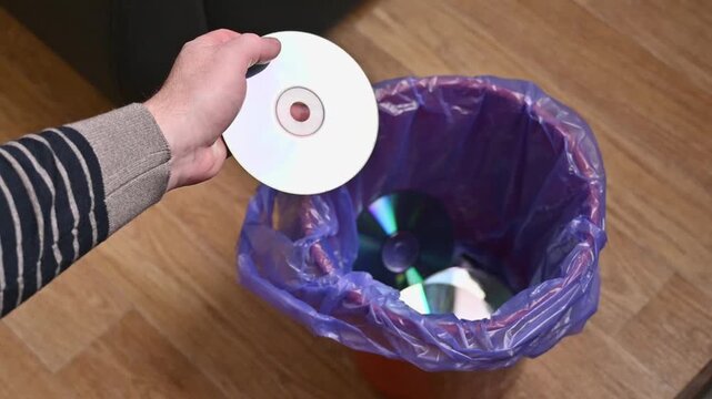 A man throws old CDs from a CD player or computer into a trash can.