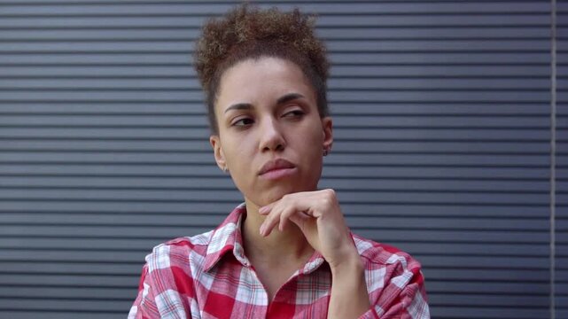 thoughtful African American woman plans and thinks against the backdrop of urban wall, unsure girl dreams and imagines solution and chooses outdoors