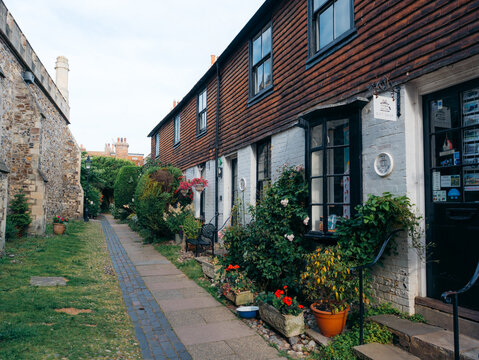 Rye, United Kingdom - 23 June 2025: View of a charming row of historic cottages with vibrant flower boxes and brick rooftops along a quaint cobblestone path.
