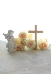 Naklejka premium Religion background. Beautiful angel figurine with wooden cross and rose flowers on table close up. symbol of Easter holiday, Christianity religion, faith in God, prayer, memory. soft focus