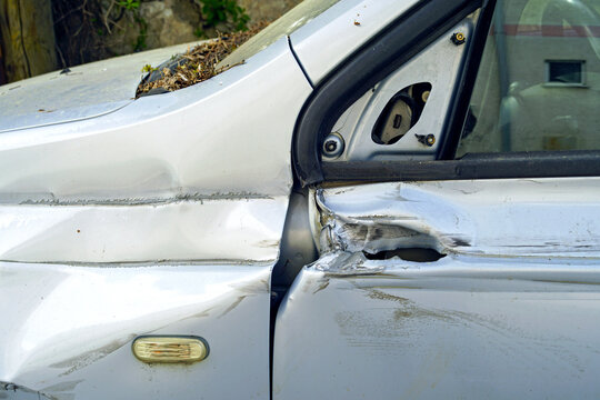 Bent vehicle frame section near door hinge with severe structural distortion in outdoor setting. Represents safety concerns, compromised integrity, and hidden damage risks after side collision events.