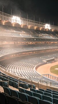 Vertical video: Turning on stadium lights bathing empty curved seats to light stands, haze drifting