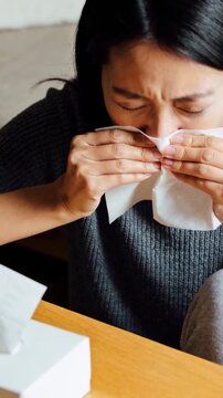 Vertical video: Woman sniffling by table tissue box, wiping, unfolding, pressing tissue for health