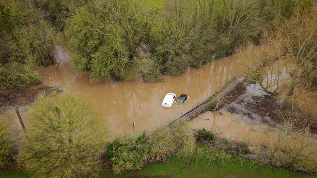 Hurricane flooding submerging cars on rural road after extreme storm. Powerful storm surge covering countryside bridge and trapping vehicles in muddy water. Natural disaster causing severe transport