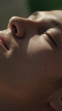 Vertical video: Breathing male in profile, cheek rising, eye twitching, resting in bed, green blur