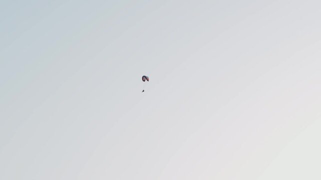 Solo paramotor pilot drifting through vast pale sky minimal composition high altitude powered paragliding flight. Extreme paramotoring activity continuing steady glide in open atmosphere adventure