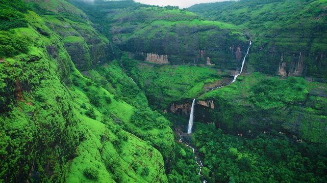 4K Aerial shot of Lush green hills and Ring waterfall as seen from Savalya Ghat view point in Maharashtra, India. Bird's eye view of Sahyadri hills during rainy day. Travel background. Waterfall and c