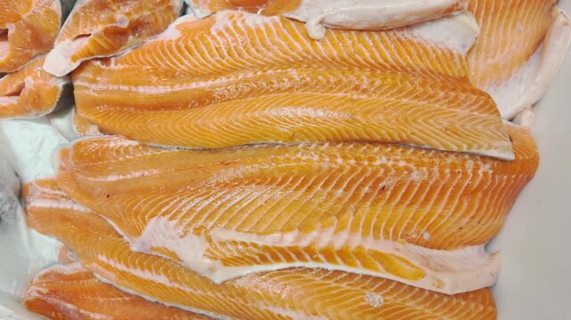 Fresh raw salmon fillets with bright orange flesh and white fat layers are stacked together. The succulent fish texture highlights the high quality of the seafood product.