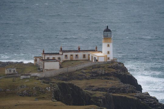 View of a Neist Point Lighthouse standing tall against the turbulent sea, its white facade contrasting with the dark cliffs, a beacon of hope, Isle of Skye, Scotland.