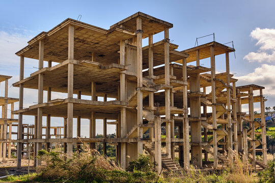 View of unfinished concrete building skeleton rises against a pale blue sky with scattered clouds, a testament to halted construction, Manilva, Andalusia, Spain.