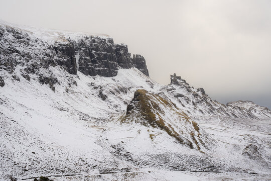 View of snow-dusted mountains and rugged terrain meet a soft, overcast sky, painting a serene yet dramatic landscape, Quiraing, Isle of Skye, Scotland.