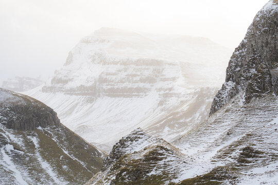 View of snow-dusted peaks and valleys under a soft, diffused light, creating a tranquil yet powerful scene of nature's grandeur, Quiraing, Isle of Skye, Scotland.
